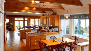 A spacious kitchen with wooden beams, a large island, and a dining area with chairs. - Dramatic Oceanfront House w/ Private Swimming Cove & Dock (Freeport)