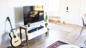 Sala de estar con televisor, guitarra, otoman y dos mesas redondas.