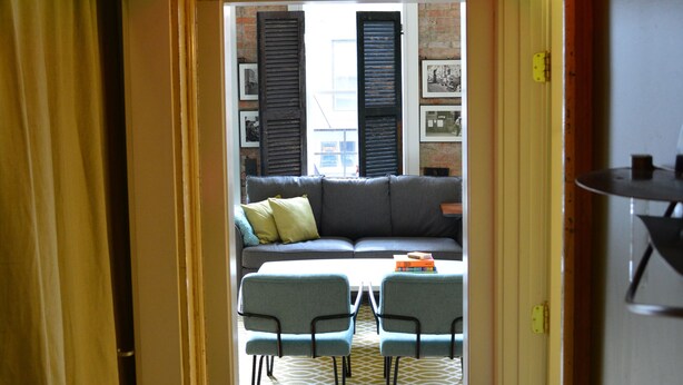 Un couloir mène à un espace de vie comprenant un canapé, des fauteuils et une table.