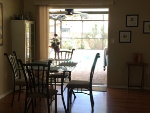 Enjoy meals in this dining area with a glass-top table and four chairs, surrounded by a large window and a ceiling fan.