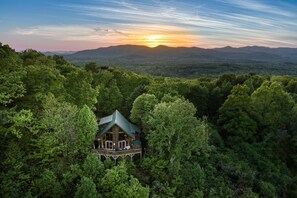 A cabin surrounded by dense forest, with a view of distant mountains and a sunset. - Soaring Hawk The `Ultimate` Log Cabin with EPIC Breathtaking Views|Hot Tub|Pets Welcome (Sautee Nacoochee)