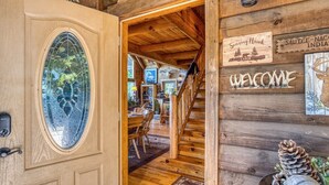 Een houten cabin met een deur van glas-in-lood, een trap en een bord met een welkomstboodschap.