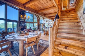 A wooden interior with a dining area, large windows, and a staircase. - Soaring Hawk The `Ultimate` Log Cabin with EPIC Breathtaking Views|Hot Tub|Pets Welcome (Sautee Nacoochee)