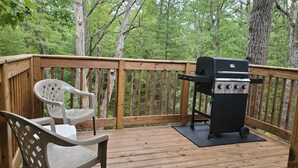 A wooden deck with a grill and a plastic chair.