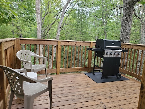 A wooden deck with a grill and a plastic chair.