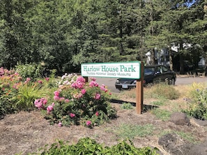 Schild für Harlow House Park, umgeben von einem Garten mit rosa Blumen und einem geparkten Auto.