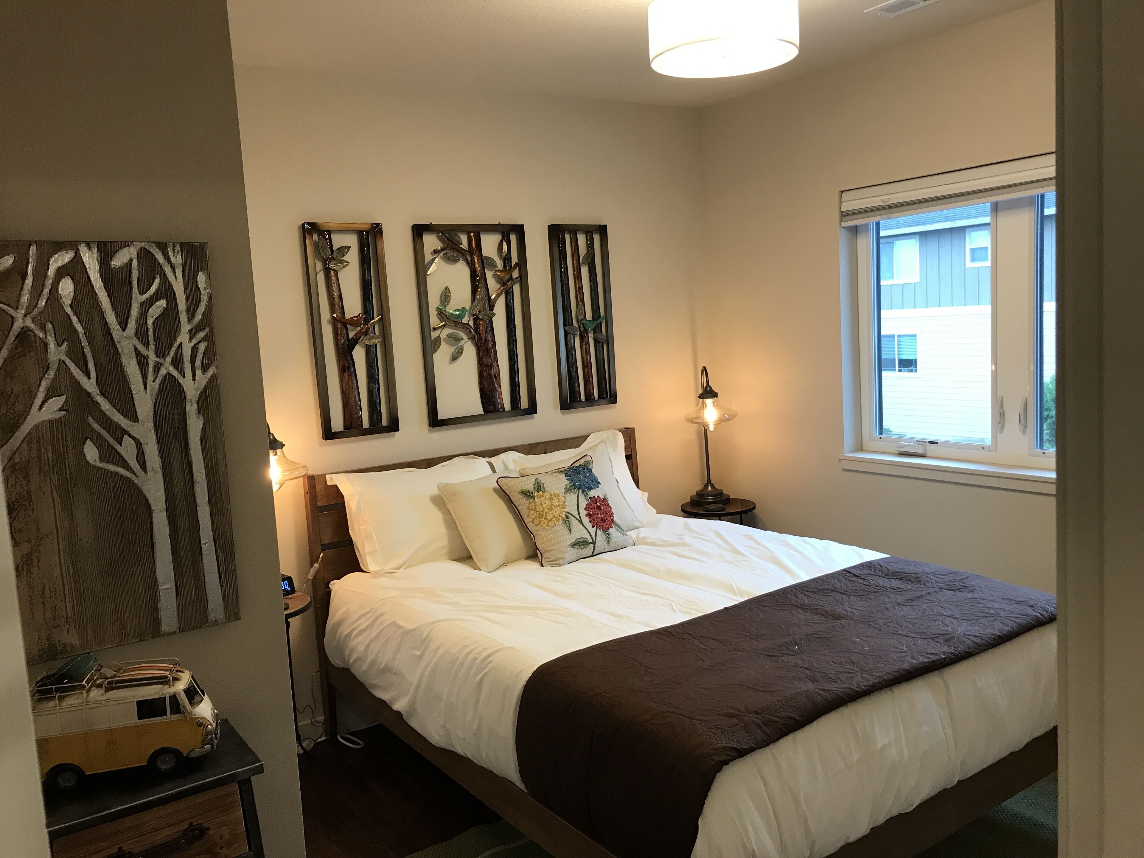 A bedroom with a bed, a nightstand, a lamp, a window, and wall art.