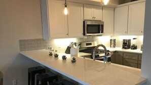 Une cuisine moderne avec des armoires blanches, un four à micro-ondes en acier inoxydable, une cuisinière à gaz et un grand îlot central doté de tabourets de bar.