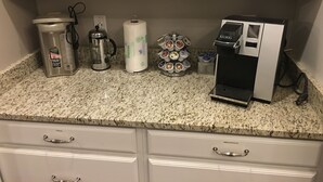 A kitchen with a coffee maker, a French press, a paper towel holder, and a coffee pod dispenser.