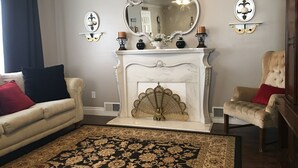A living room with a white fireplace, two armchairs, a sofa, and a large mirror.