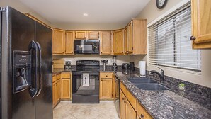 A kitchen with wooden cabinets, a stainless steel refrigerator, a microwave, a stove, a sink, and a clock on the wall.