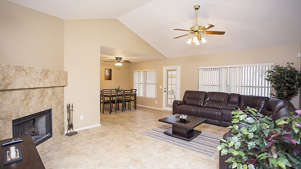 A living room with a fireplace, a brown leather sofa, a coffee table, and a ceiling fan.