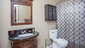 A bathroom with a wooden vanity, a sink, a mirror, a toilet, and a shower curtain.