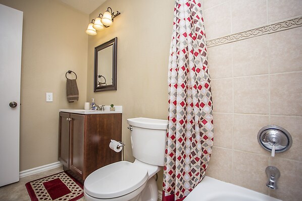 A bathroom with a toilet, sink, cabinet, and shower curtain.