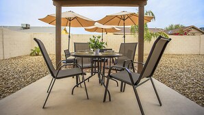 An outdoor patio with a round table, four chairs, and two umbrellas.