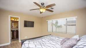 A bedroom with a bed, a ceiling fan, a TV, and a window with blinds.
