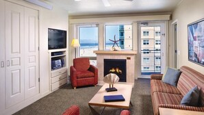 A living room with a fireplace, a television, a red armchair, and a sofa. - Luxury Vacation Condos at Seaside Oceanfront Resort (Seaside)