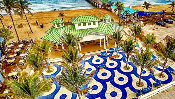 A resort with a beach view, a pier, and a pool area with palm trees.