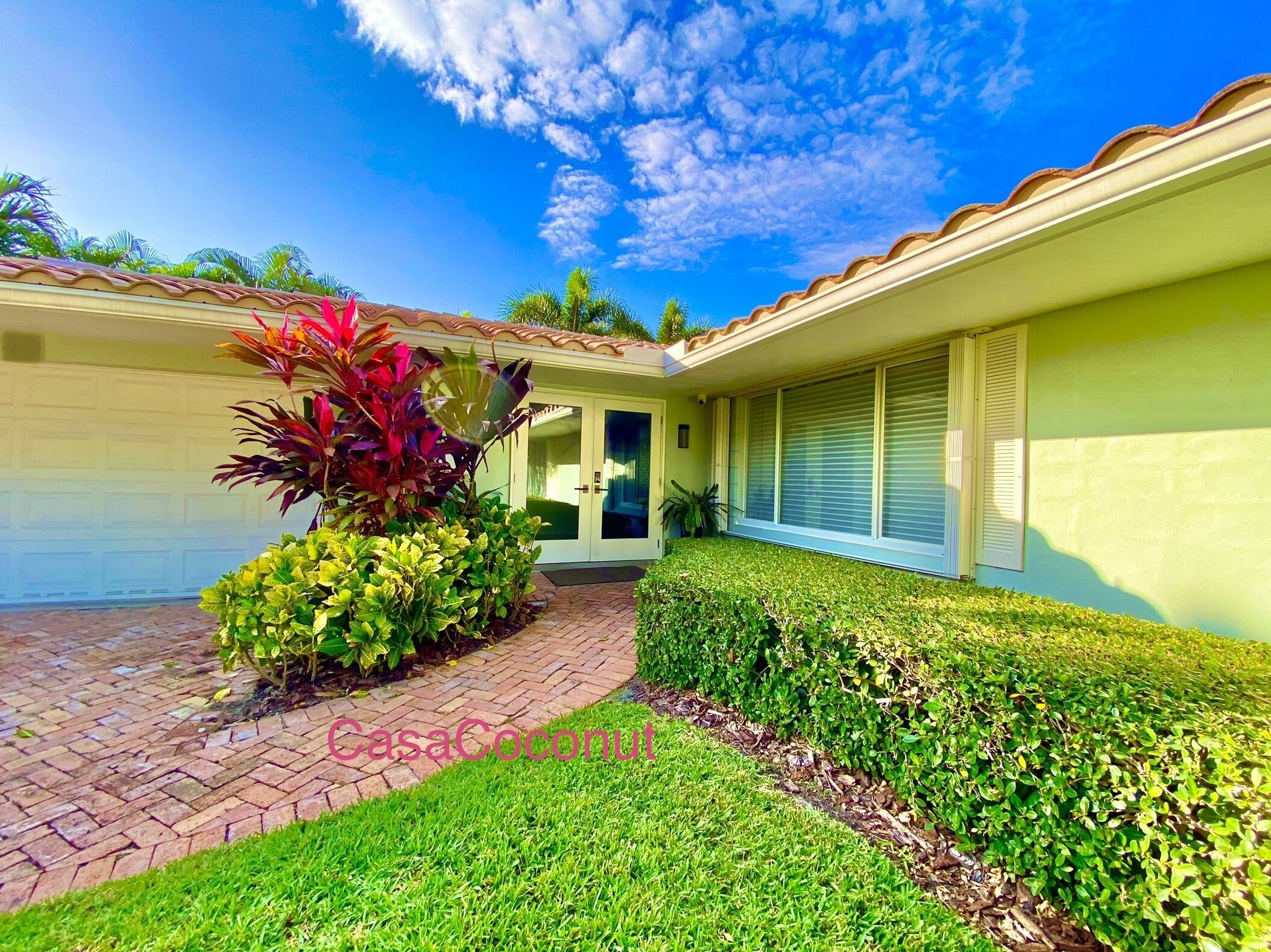 A house with a paved driveway, a well-maintained lawn, and a variety of colorful plants.
