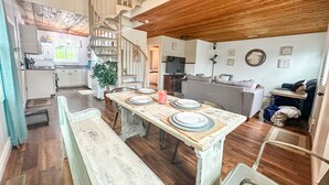 Une cuisine spacieuse avec un plafond en bois, un coin repas doté d’une grande table pour quatre personnes et un escalier en colimaçon menant à un niveau supérieur.