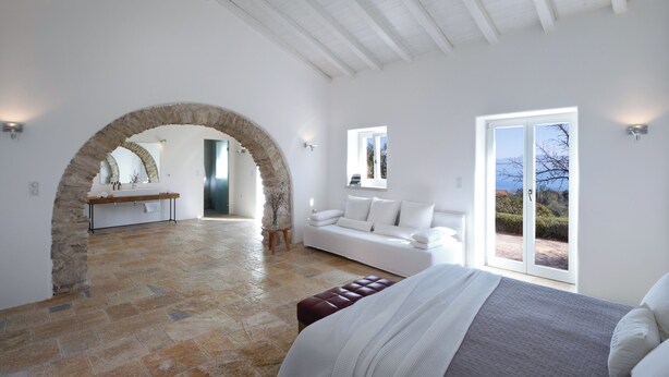 Une chambre spacieuse avec une arche en pierre menant à une salle de bain, une grande fenêtre offrant une belle vue et un coin salon confortable.