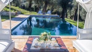 Un cadre agréable au bord de la piscine, avec une table dressée pour deux, entourée de chaises longues blanches, et une vue dégagée sur la piscine.