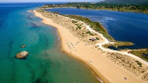 Vue aérienne d’une zone côtière avec une plage de sable, des eaux d’un bleu limpide et une route qui longe le rivage.