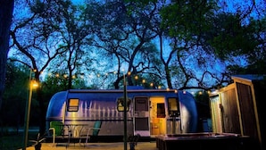Ein Wohnwagen mit einer kleinen Terrasse, einem Tisch und Stühlen, umgeben von Bäumen und Lichterketten.