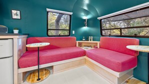 Ein kompakter Raum mit türkisfarbenen Wänden, einem roten Sofa, einem kleinen Tisch und einem Fenster mit Blick auf Bäume.