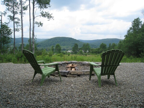 Two green Adirondack chairs facing a stone fire pit with a view of a forested mountain range. - Private 4-bedroom chalet with breathtaking views! (Great Valley)