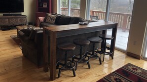 A cozy living room with a wooden bar and stools, a sofa with cushions, a television, and a bookshelf. - Private 4-bedroom chalet with breathtaking views! (Great Valley)