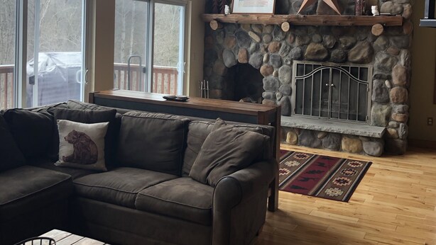 A cozy living room with a stone fireplace, a large window, and a wooden ceiling. - Private 4-bedroom chalet with breathtaking views! (Great Valley)