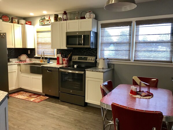 Una cocina compacta con armarios blancos, electrodomésticos de acero inoxidable y una mesa de comedor roja.