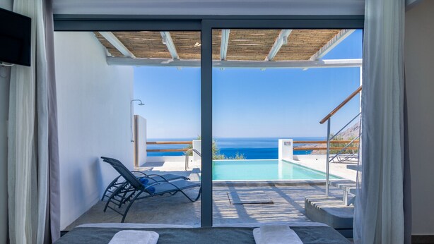 A room with a bed, towels, a view of the sea, and a pool area. - Pyrgos Exclusive 2, Sea View & Private Pool (Plakias)