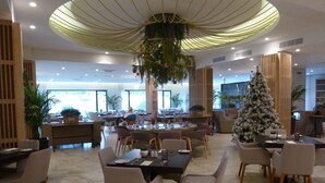 Un vaste espace dédié à la salle à manger, avec de nombreuses tables et chaises, un grand sapin de Noël et un design moderne au niveau du plafond.