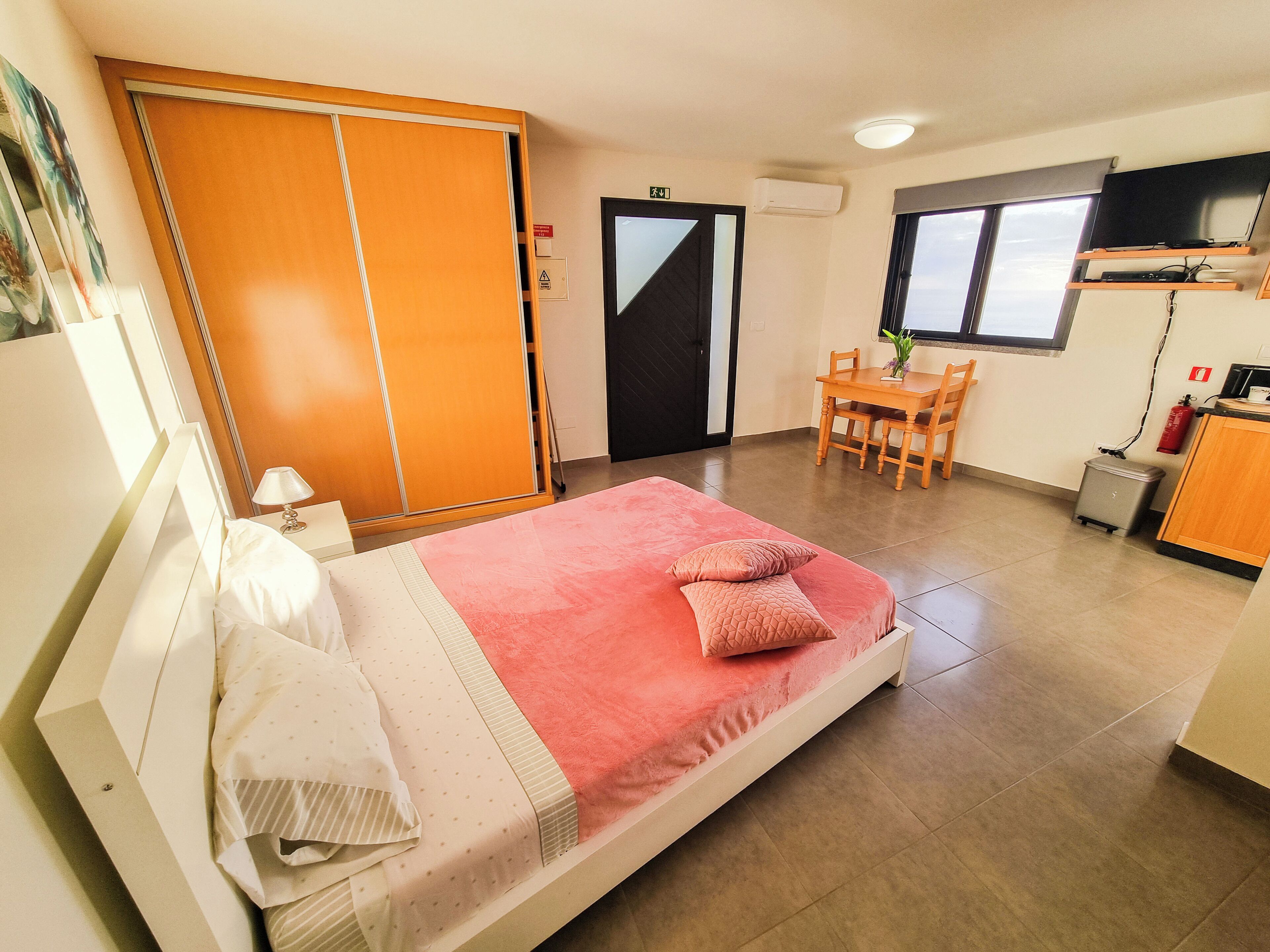 Ein Schlafzimmer mit Bett, Schreibtisch und Stuhl. Es gibt einen Kleiderschrank, eine Tür und ein Fenster.