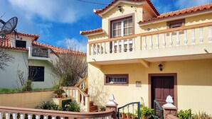Une maison à deux étages avec un balcon, une porte d’entrée et un portail.