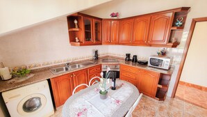 Une cuisine avec des meubles de rangement en bois, un lave-linge, un four à micro-ondes et une table à manger avec des chaises.