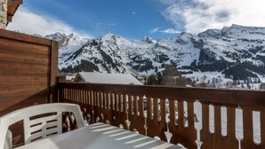 Een houten balkon met een witte tafel en stoelen, met uitzicht op besneeuwde bergen en een helderblauwe lucht.