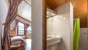 Een slaapkamer met een houten plafond, een bed met een geruite deken en een raam met gordijnen.