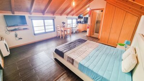 A spacious room with a large bed, wooden ceiling beams, a dining area, and a kitchenette. - Studio One | Ocean View | Perfect Budget Couple's Retreat with Free WIFI (Fajã da Ovelha)