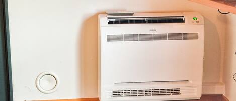Een witte airconditioner in een hoek van een kamer met houten vloeren en een witte muur.