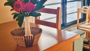 A wooden table with a white vase containing pink flowers and green leaves. - Studio One | Ocean View | Perfect Budget Couple's Retreat with Free WIFI (Fajã da Ovelha)