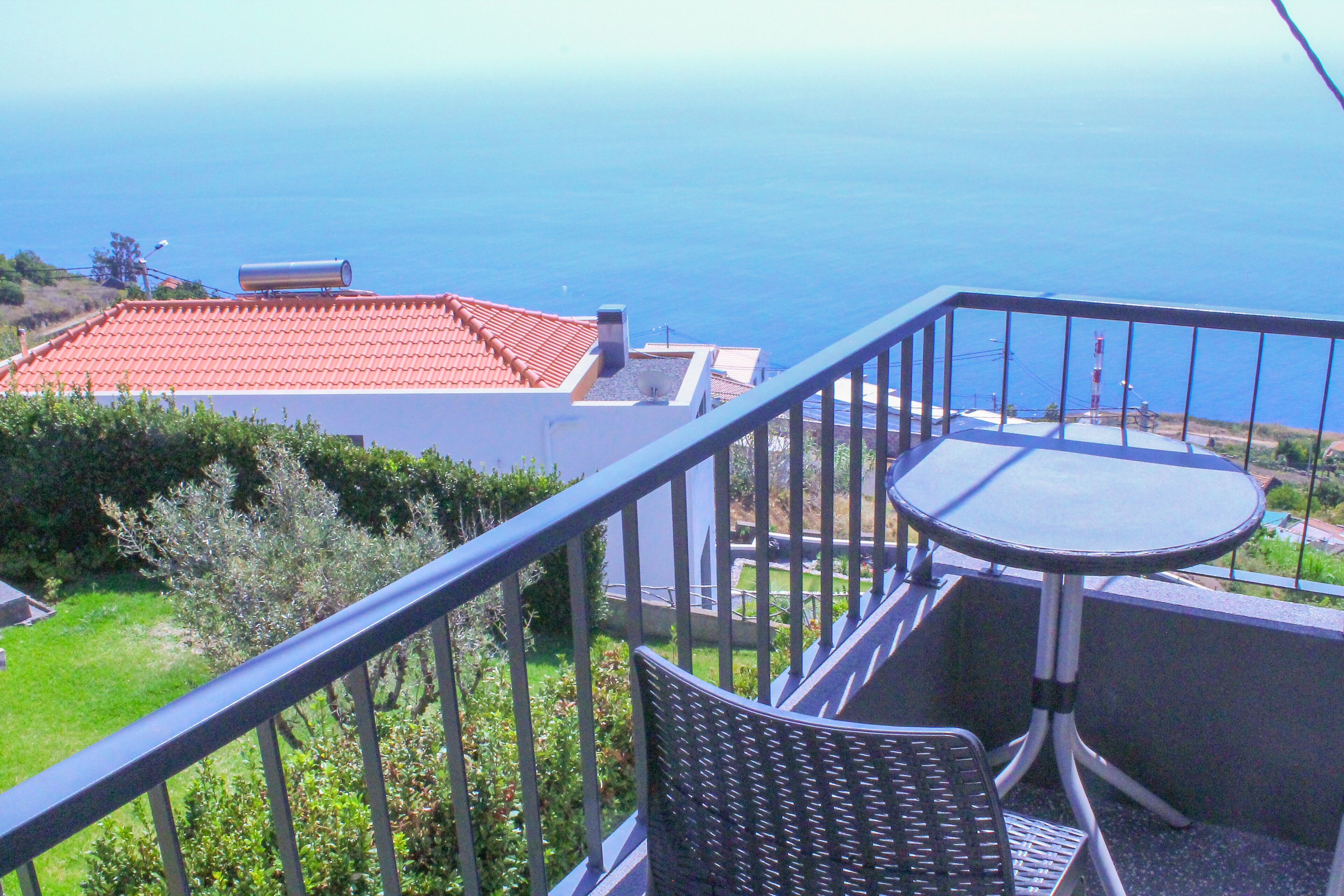 A balcony with a view of the sea, a table, and a chair.