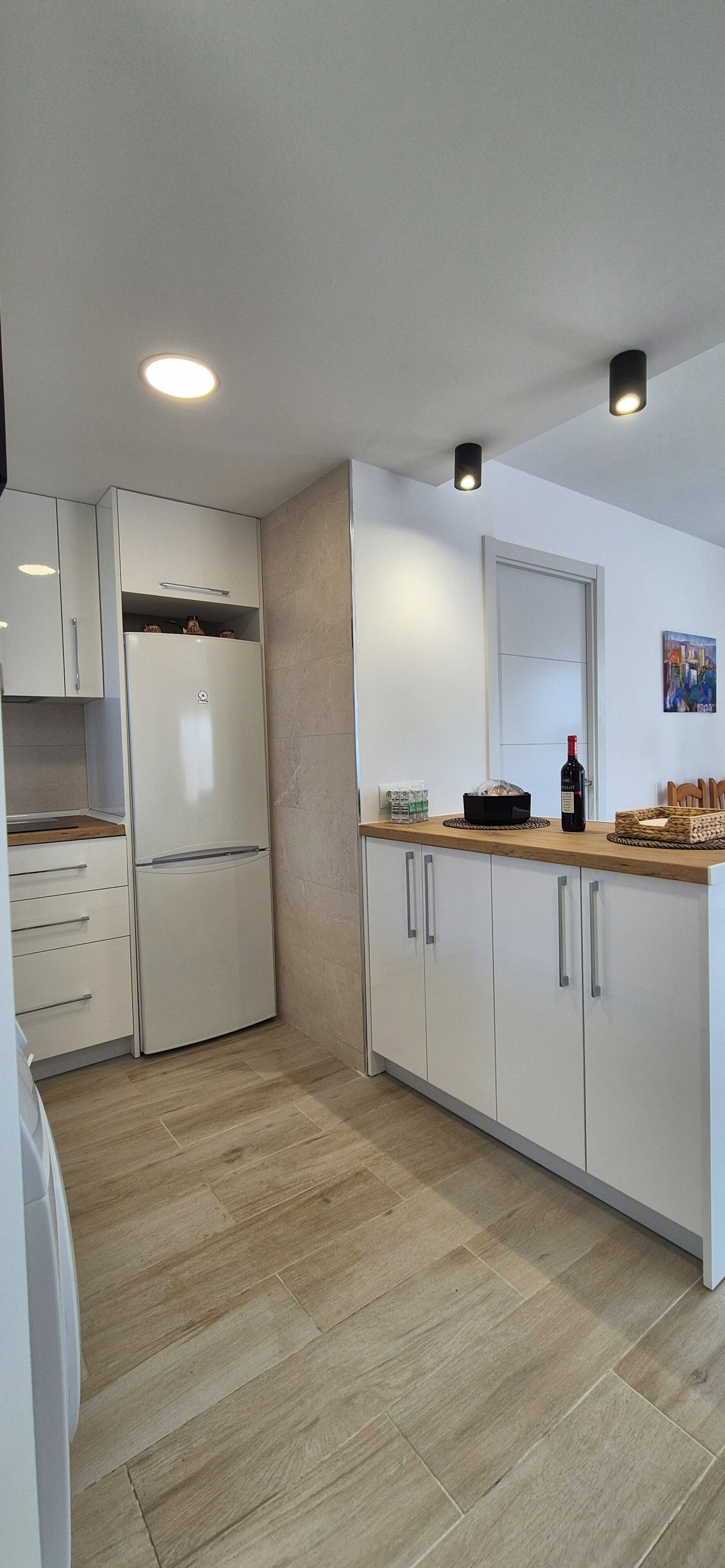 A modern kitchen with white cabinets, a built-in refrigerator, and a wooden countertop.