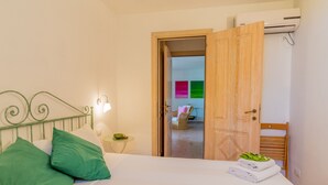 Ein Schlafzimmer mit einem Bett, Kissen, einem Nachttisch, einer Lampe und einer geöffneten Tür zu einem Badezimmer.