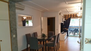 Spiseområde med et glasbord og stole, et fjernsyn samt udsigt til terrassen.