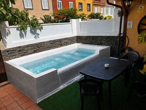 Un jacuzzi rectangulaire bordé de pierres, avec une table et des chaises, situé dans un espace patio.