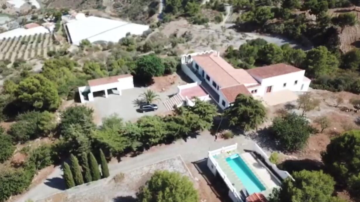 An aerial view of a property with a swimming pool, a two-story building, and surrounding greenery.