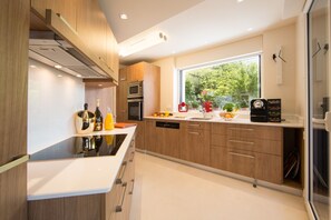 A modern kitchen with wooden cabinets, a built-in oven, and a window providing a view of greenery outside. - Villa Bagatelle 5 stars Vision Luxe 10 people 5 bedrooms Annecy (Veyrier-du-Lac)